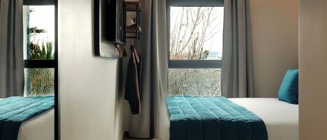 A modern hotel room with two beds, a TV mounted on the wall, and a window with curtains.