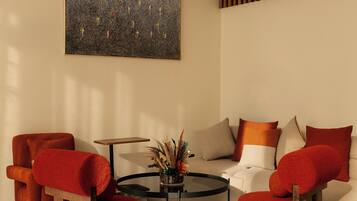 A modern living room with a round coffee table, red and beige armchairs, a sofa with orange cushions, and a large abstract painting on the wall.