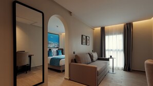 Una camera d'albergo moderna con un letto grande, un divano, un tavolino e uno specchio ampio.