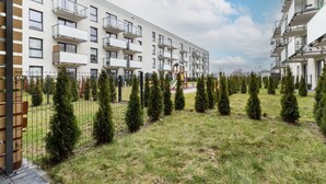 A modern apartment building with multiple balconies and a fenced courtyard with neatly trimmed trees.
