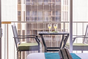 A balcony with two chairs and a table, each with a glass of drink, and a sign warning against hanging items on the railing. - "Windjammer" Studio w/FREE parking & Full Kitchen (Honolulu)