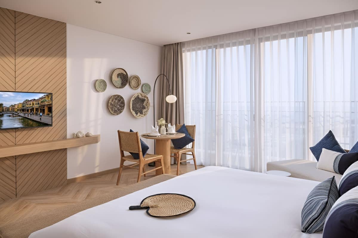 A modern hotel room with a large bed, a dining area with a round table, and a TV mounted on a wooden wall.