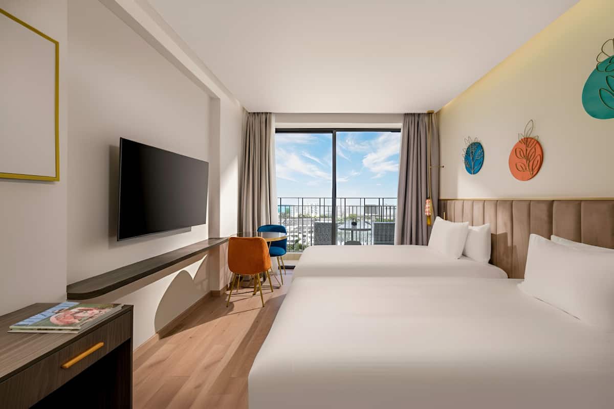 A hotel room with a large bed, a desk with a flat-screen TV, a balcony with a view, and decorative wall art.