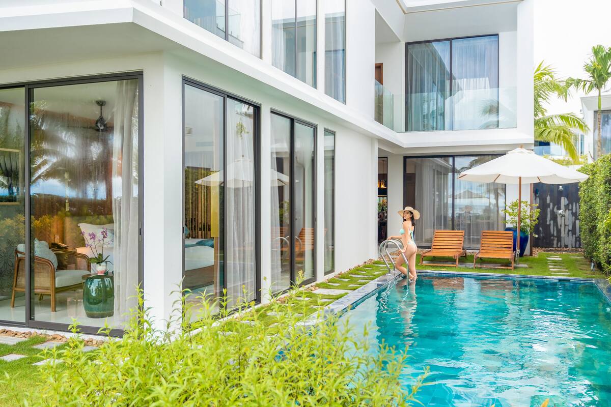 A modern poolside area with glass doors, a lounge chair, and a small garden.