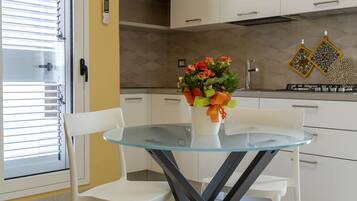 A modern kitchen with white cabinets, a glass dining table, and a flower vase.