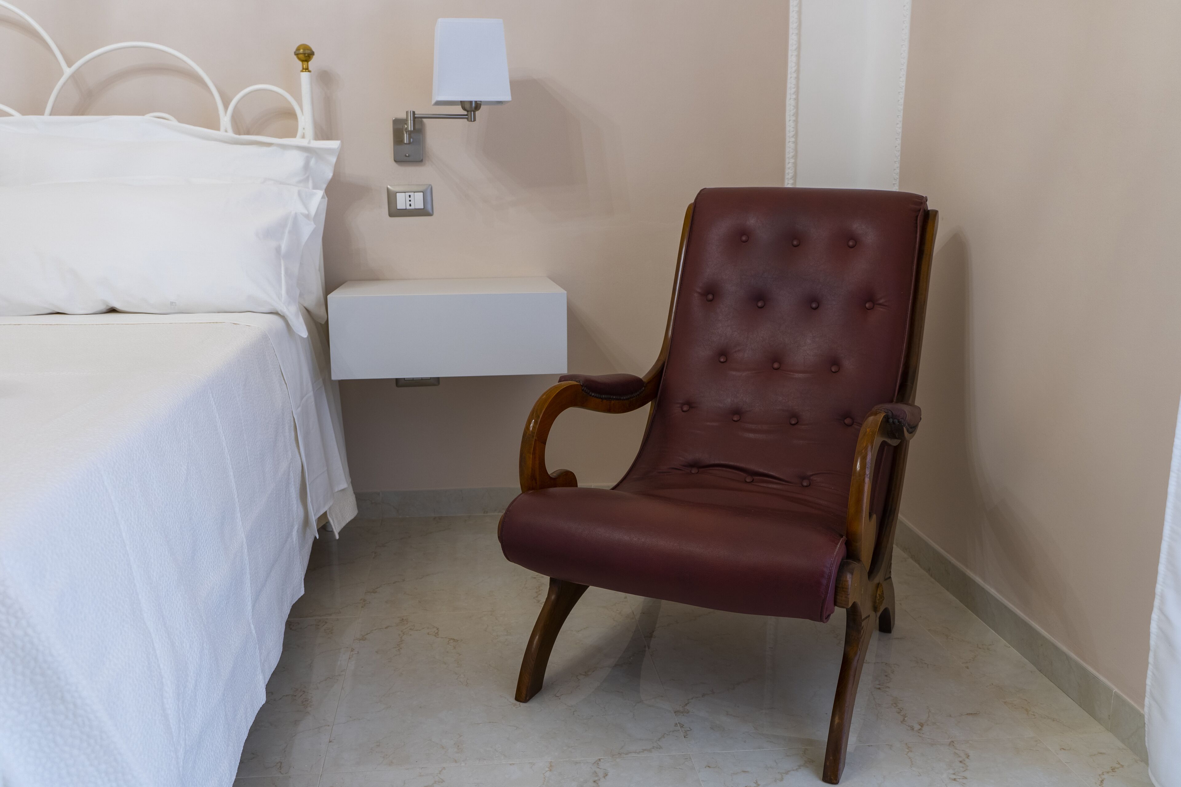 A bedroom with a bed, a nightstand, a lamp, and a leather armchair.