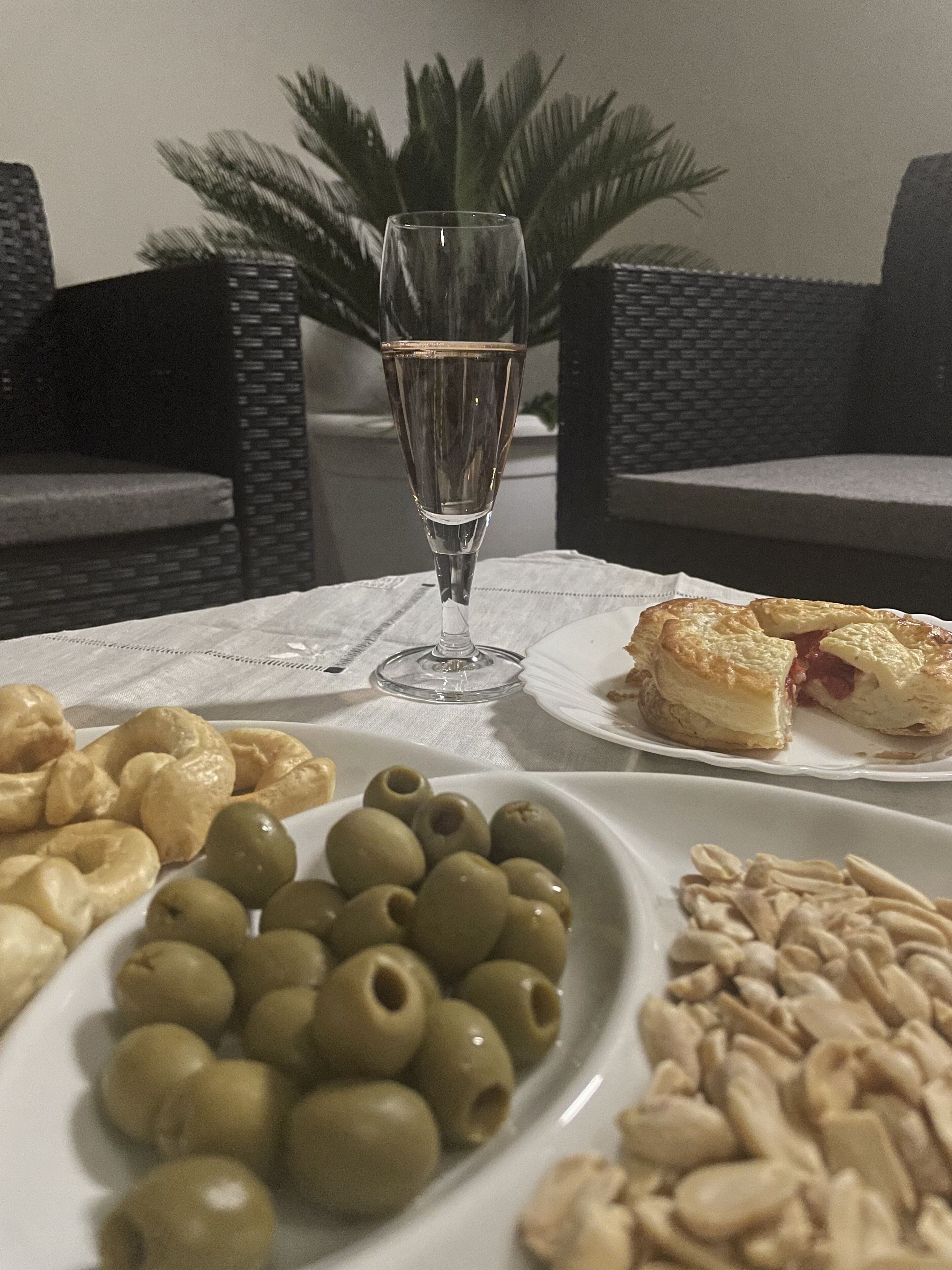 Una mesa con un vaso de agua, una fuente de aceitunas, una bandeja de pasteles y una fuente de nueces.