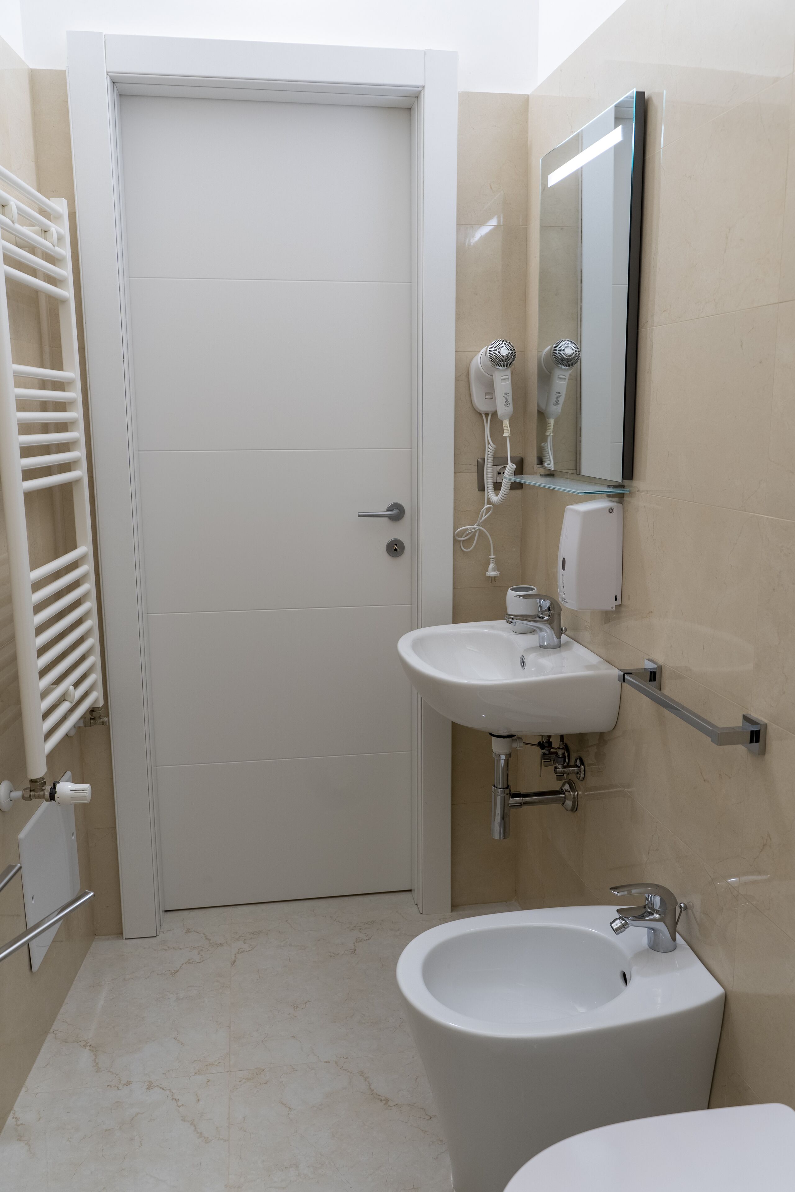 Un bagno con lavandino, bidet e WC bianchi. C'è un porta asciugamani e uno specchio a parete.