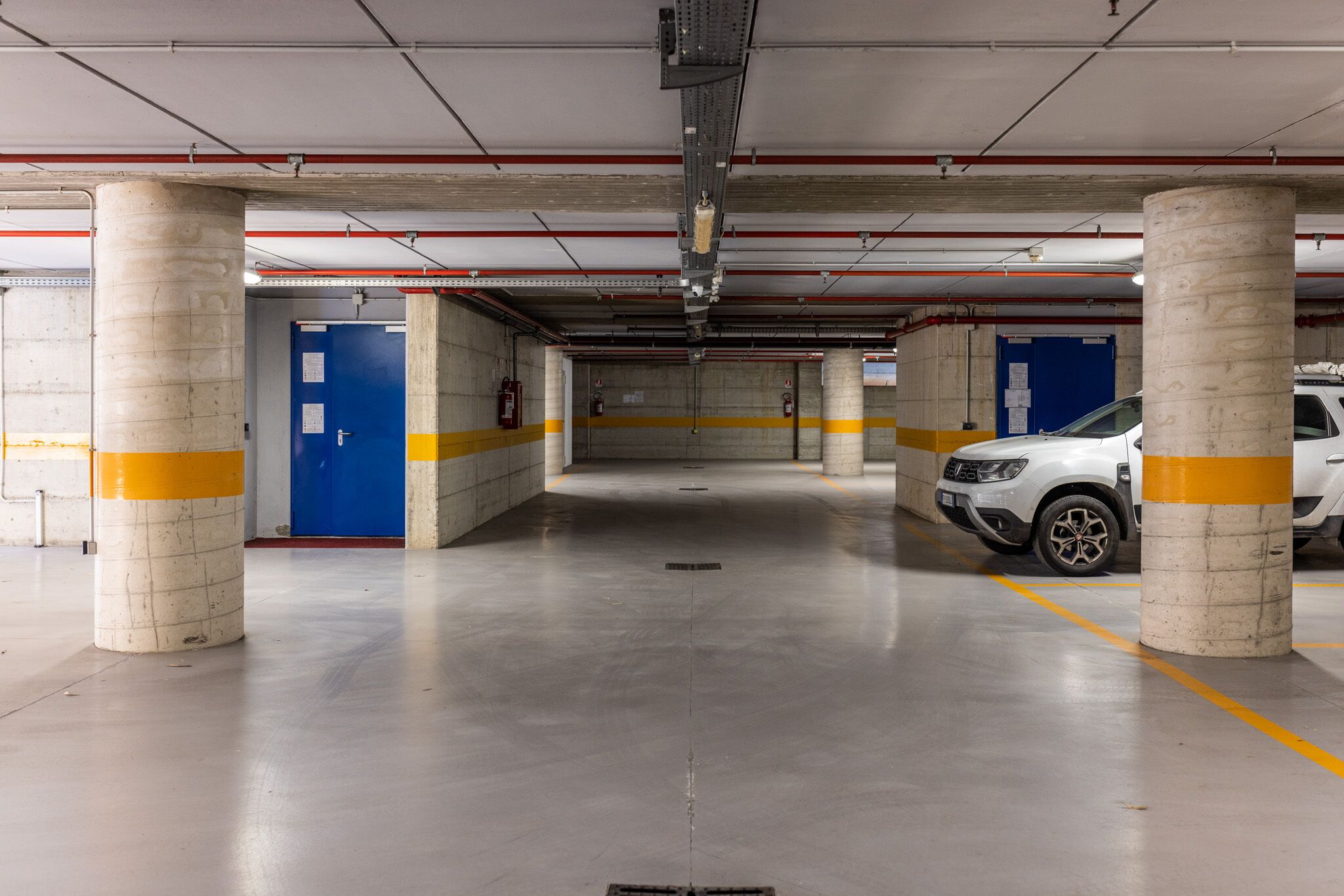 A multi-level parking garage with concrete pillars, yellow safety lines, and a white car parked.