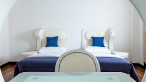 Una habitación con dos camas, cada una con cabecera blanca y almohadas azules, y una mesa de vidrio al frente.