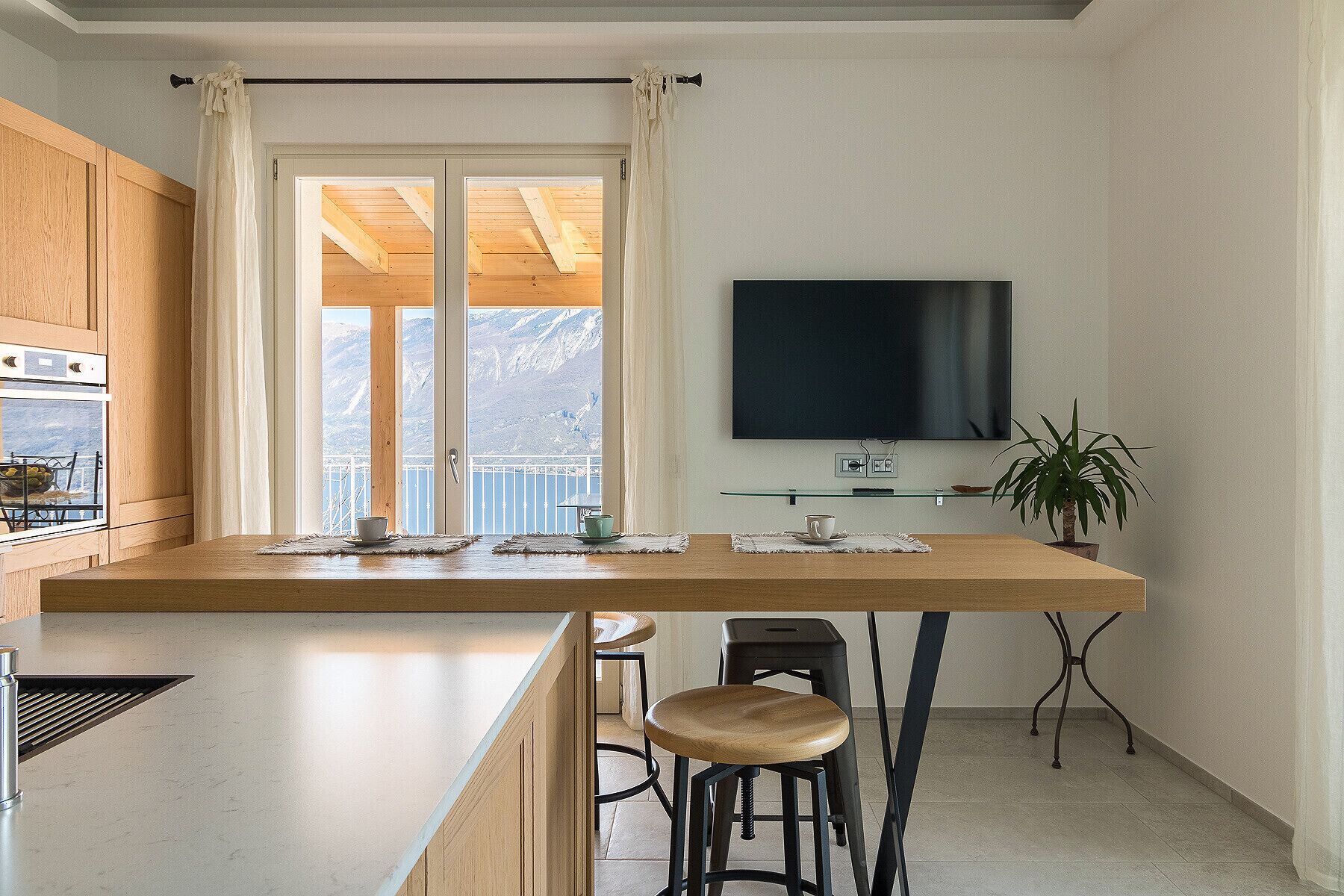 Eine moderne Küche mit großem Fenster, Holzschränken, einem Flachbildfernseher und einem Barhocker.