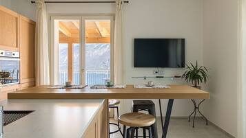 Eine moderne Küche mit großem Fenster, Holzschränken, einem Flachbildfernseher und einem Barhocker.
