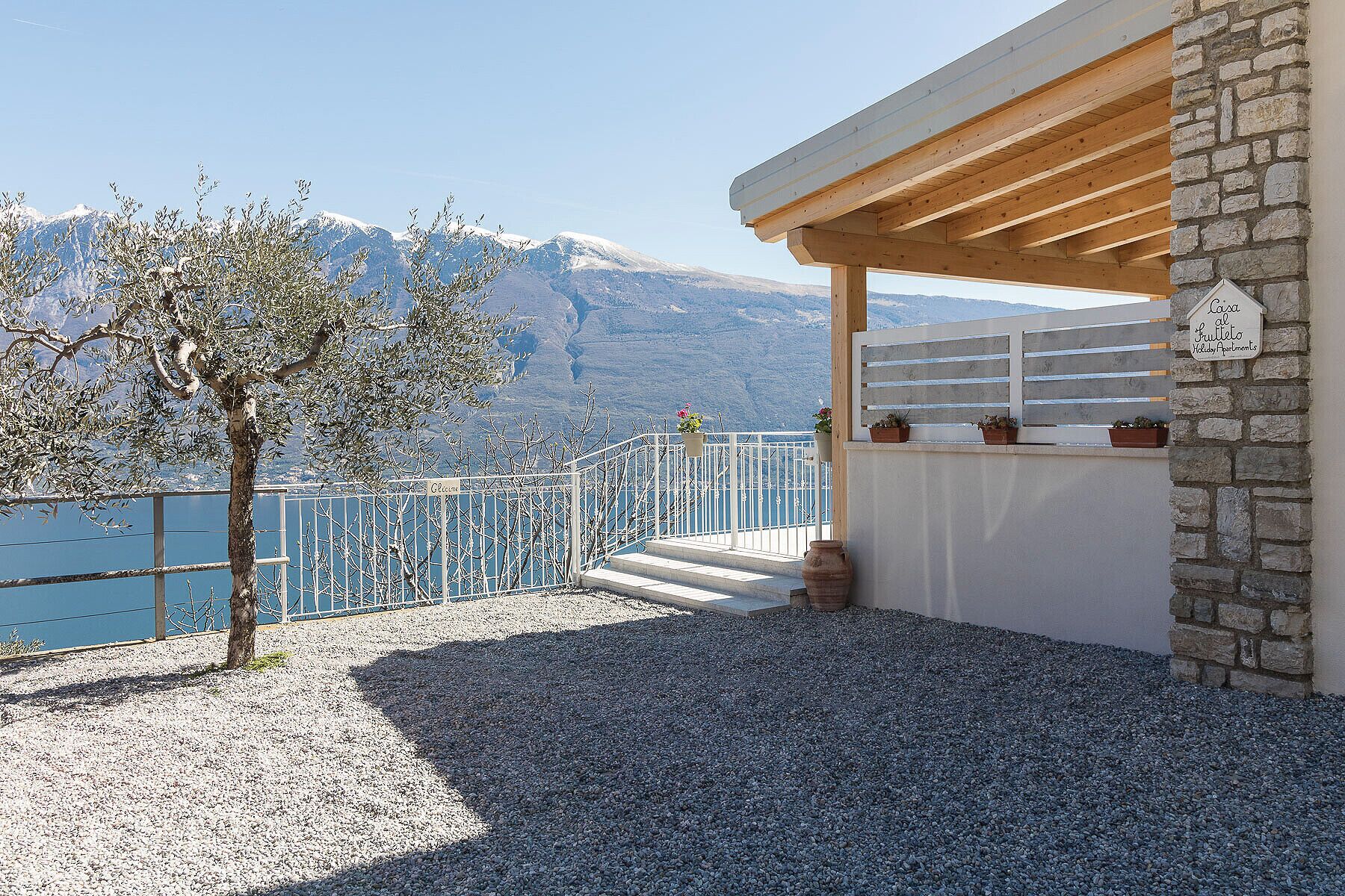 Eine Terrasse mit Steinmauer, einer Holzpergola und einem Schild, das eine Ferienwohnung kennzeichnet.