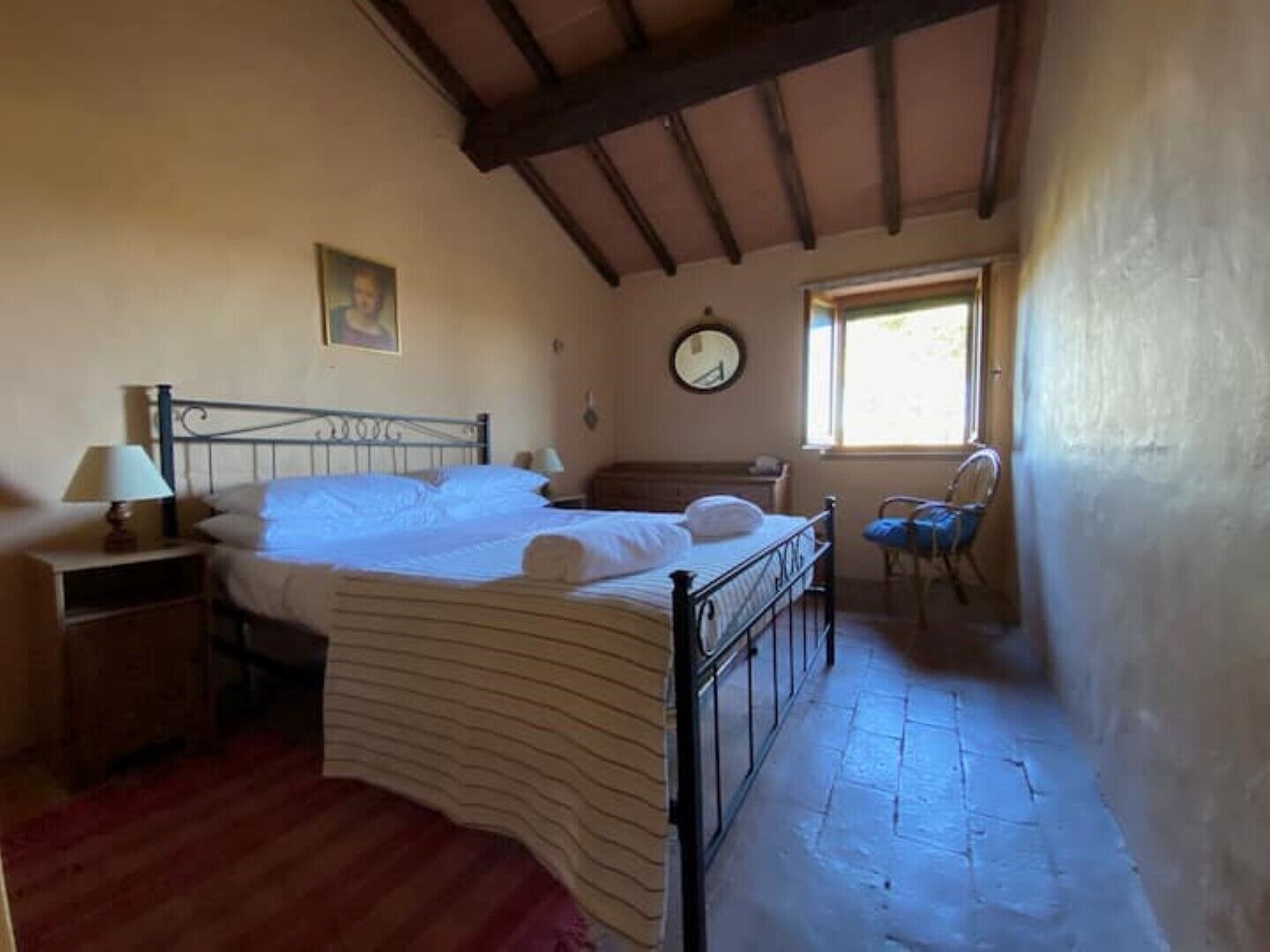 A bedroom with a bed, a nightstand, a chair, a window, and a wall clock.