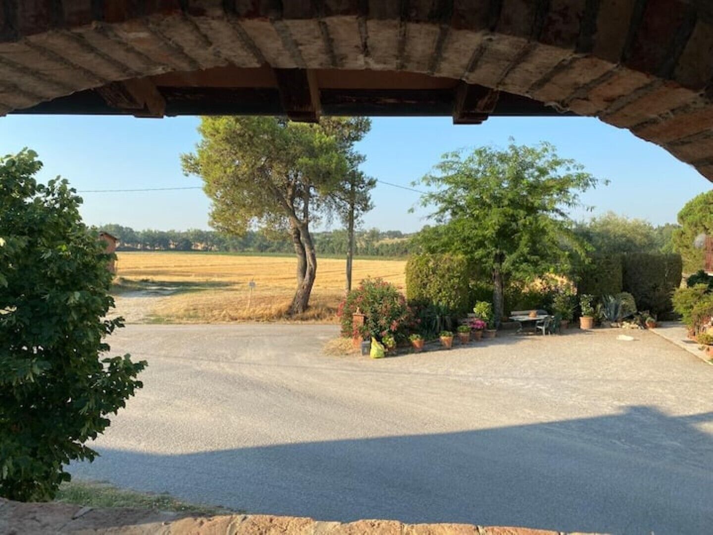 Un arco de piedra rústico con vistas a un paisaje rural, un camino de grava, árboles y una zona ajardinada.