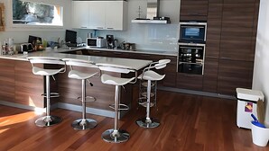 Een moderne keuken met een centraal eiland, barkrukken, een magnetron en een ingebouwde oven.