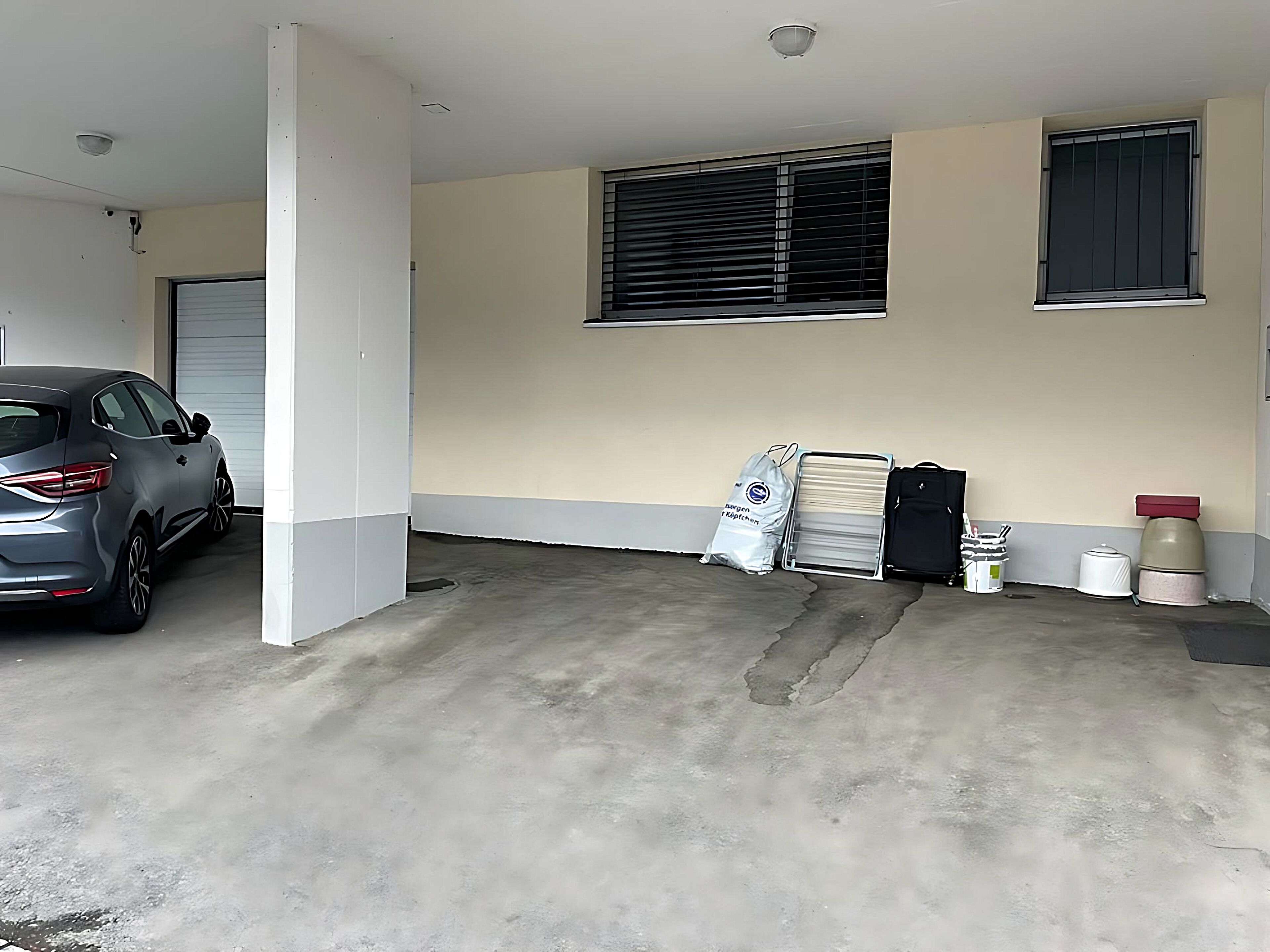 Un estacionamiento con un automóvil dentro, una ventana con persianas y algunas bolsas y contenedores en el suelo.