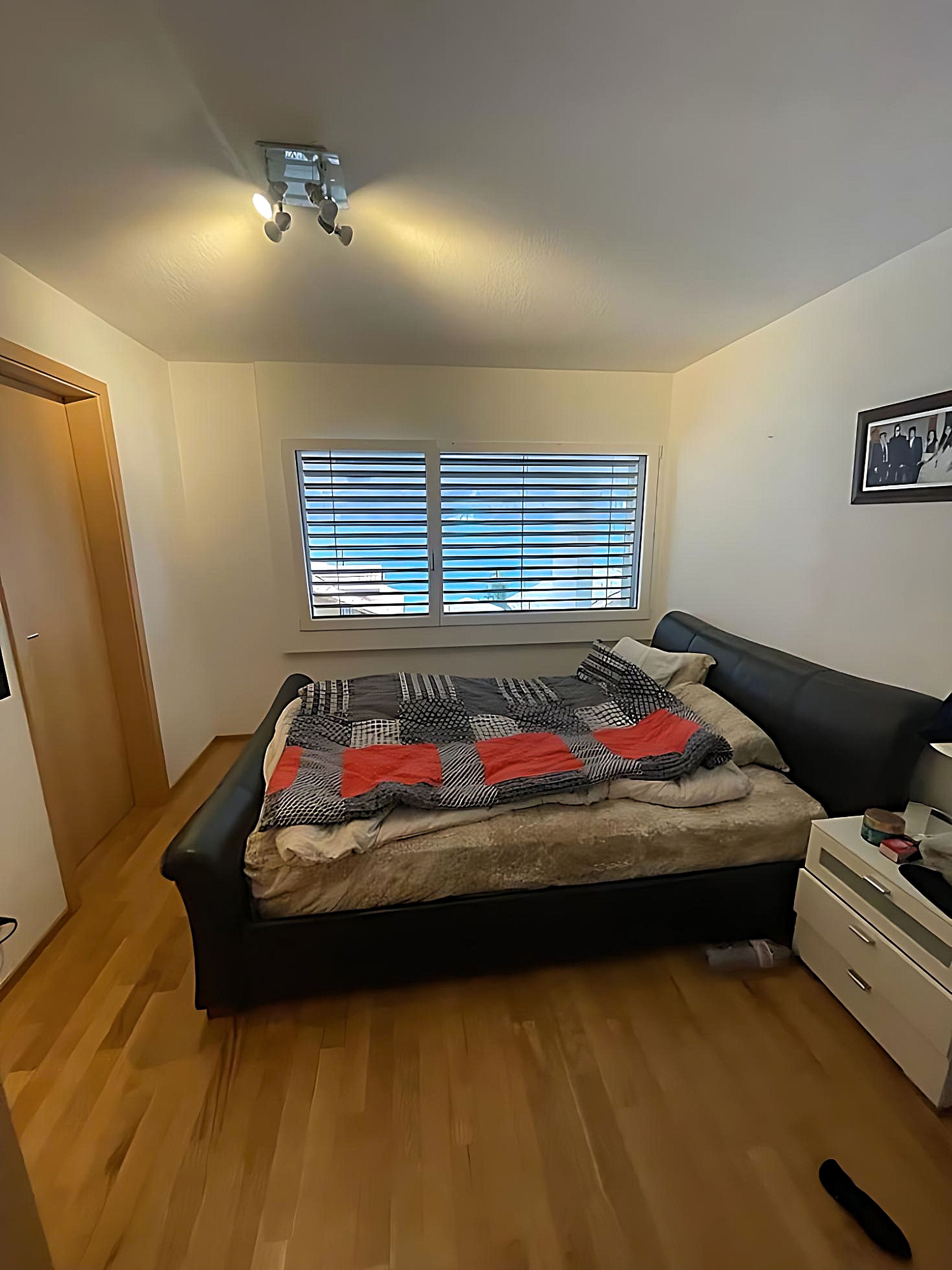 A bedroom with a bed, a nightstand, a dresser, and a window with blinds.