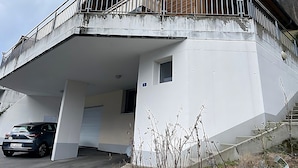 Een gebouw met een balkon, een auto ervoor geparkeerd en een trap die er naartoe leidt.