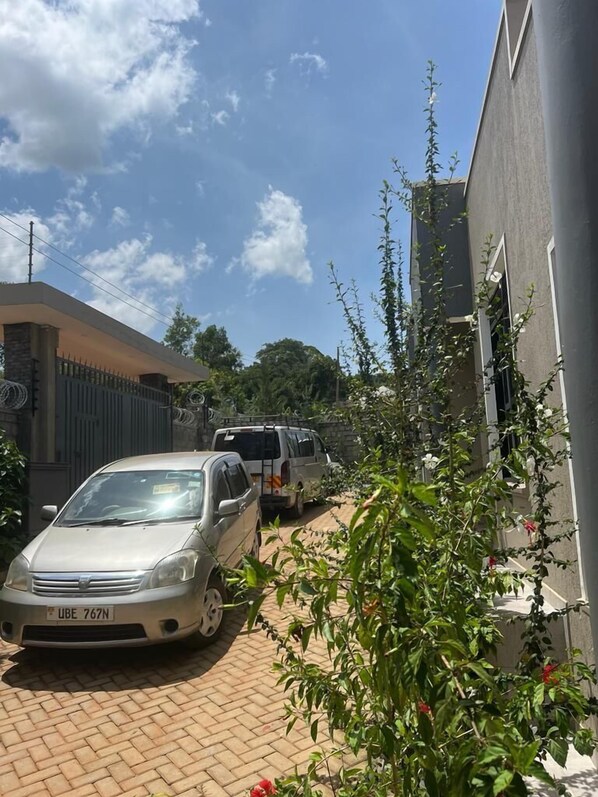 A residential area with a paved driveway, a parked silver car, and a white van. - MUNDELI HOMES LTD (Kampala)