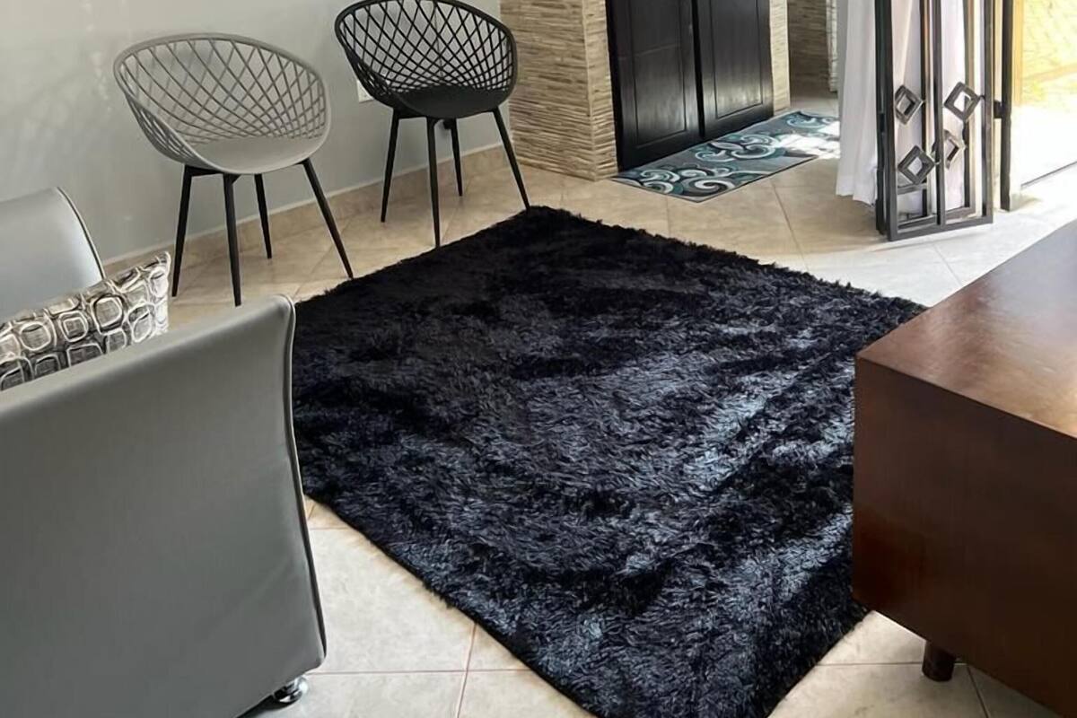 Une cuisine moderne avec des meubles sombres, un plan de travail et un évier. On y trouve deux chaises au design géométrique, un tapis noir à poils longs et un ordinateur portable posé sur le sol.