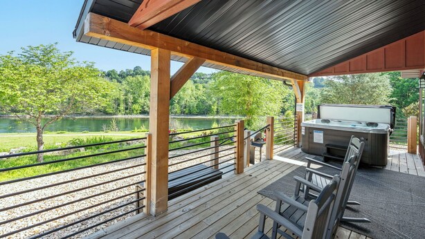 Una terraza techada con un jacuzzi, barandillas de madera y vista al lago.