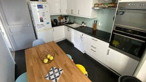 Eine kleine Küche mit weißen Schränken, einem Holztisch und einer Uhr an der Wand.