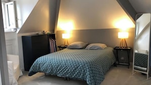Ein Schlafzimmer mit schrägen Wänden, einem Bett mit gemustertem Überwurf, zwei Nachttischlampen und einer Kommode.