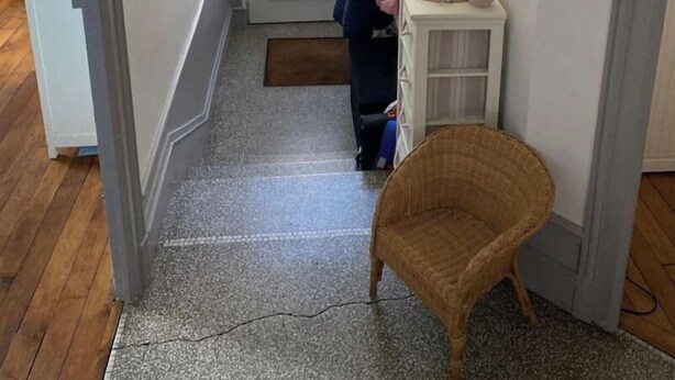 Ein Flur mit einer weißen Tür, einem kleinen Korbstuhl und einem weißen Schrank, der mit einem Hut und einer Pflanze belegt ist.
