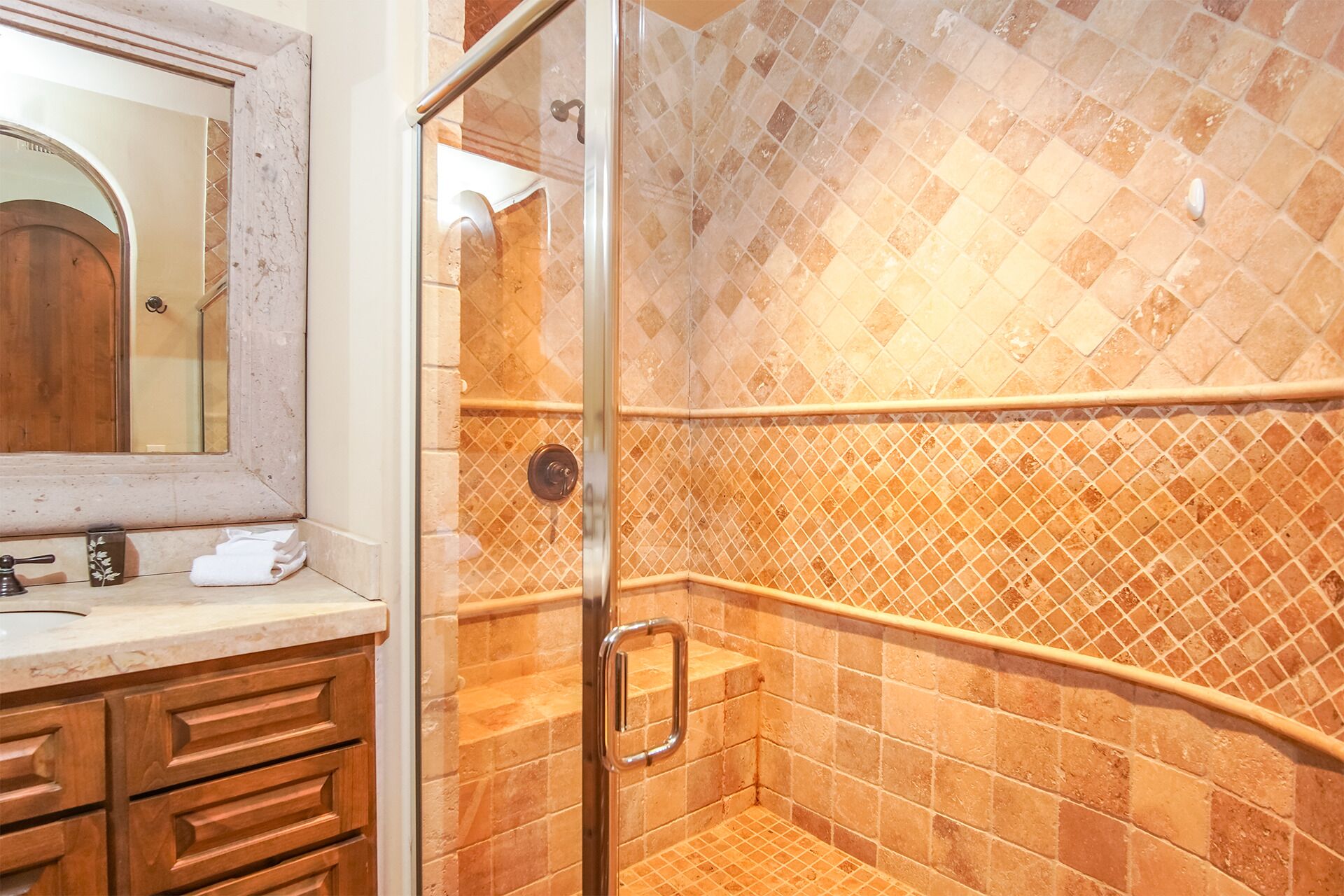 A bathroom with a glass shower enclosure, a wooden vanity, and a tiled backsplash.