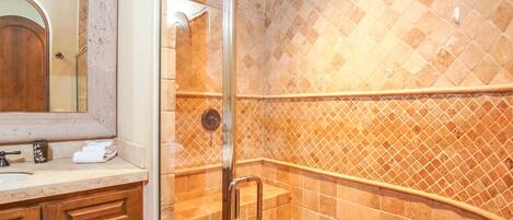 A bathroom with a glass shower enclosure, a wooden vanity, and a tiled backsplash.