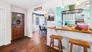 A modern kitchen with a wooden door, a welcome sign, a bar area with stools, and a view of the dining area. - Hot Tub! Pets! Green  Clean-Walking Distance to Proctor District (Tacoma)