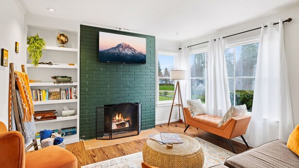A living room with a fireplace, a television mounted on a brick wall, a sofa, and a chair. - Hot Tub! Pets! Green  Clean-Walking Distance to Proctor District (Tacoma)