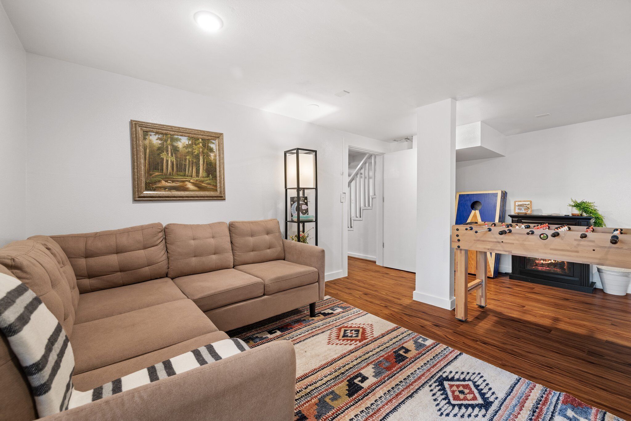 A modern living room with a sectional sofa, a patterned rug, a painting on the wall, and a foosball table.