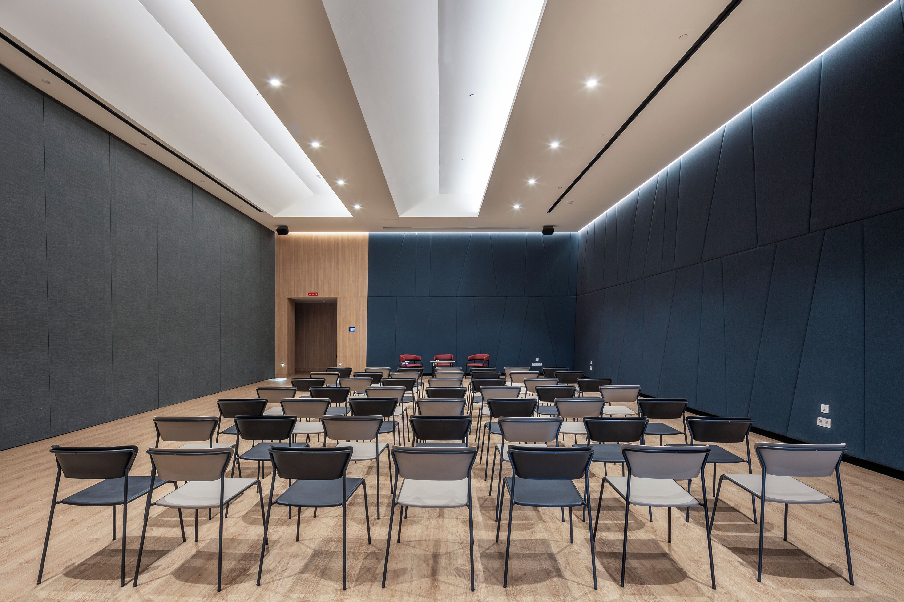 A conference room with rows of chairs and tables, a wooden door, and a dark blue wall.