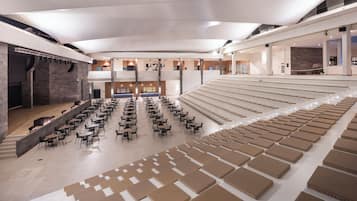 Un espacio interior amplio con asientos escalonados y mesas, un escenario y un diseño arquitectónico moderno.