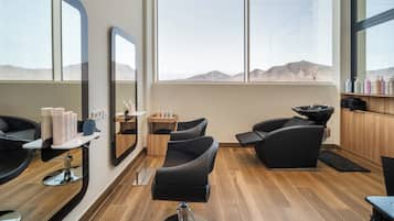 Un salón moderno con ventanas amplias, pisos de madera y sillones negros.