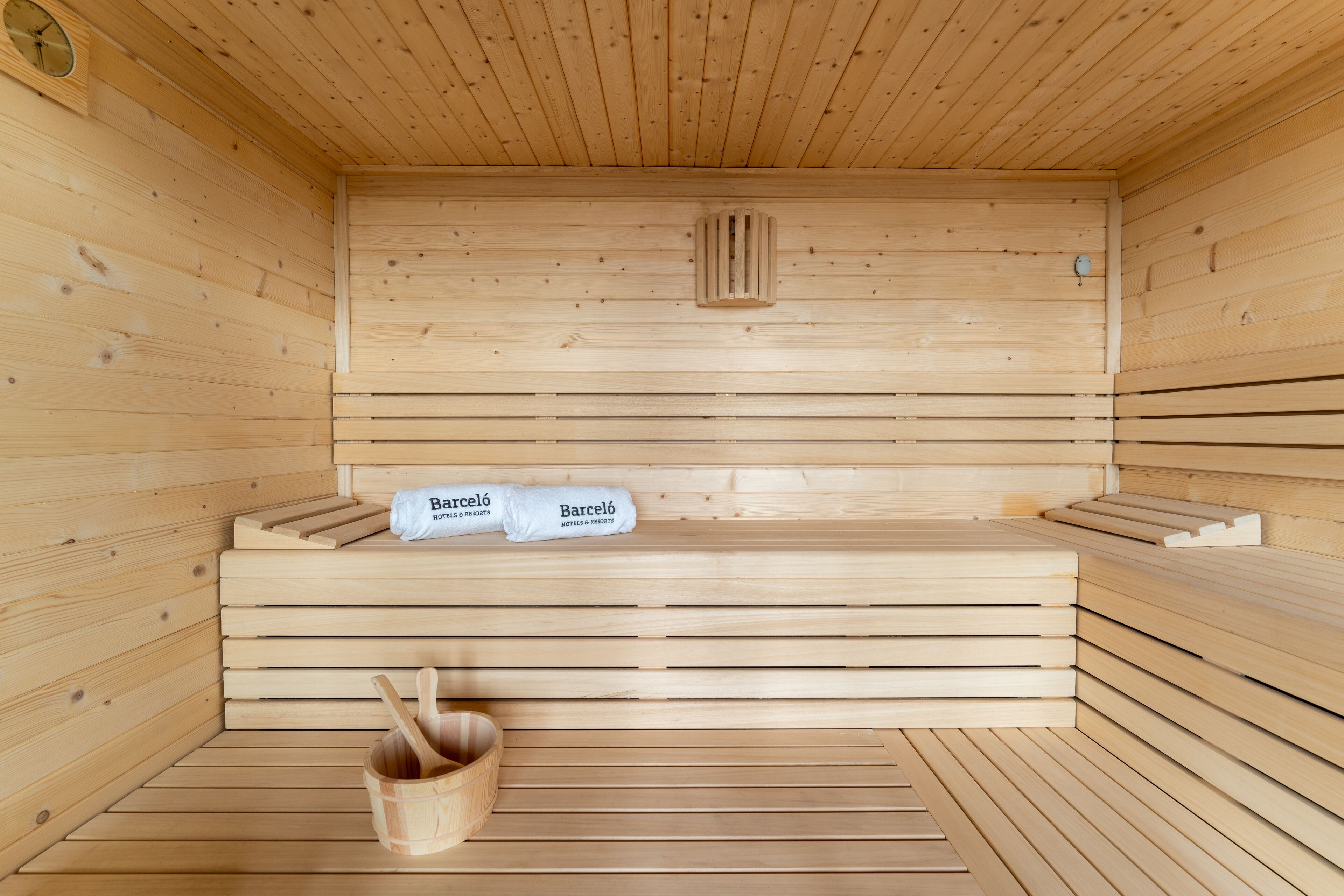 Una sauna de madera con bancos, una toalla y un balde de madera.