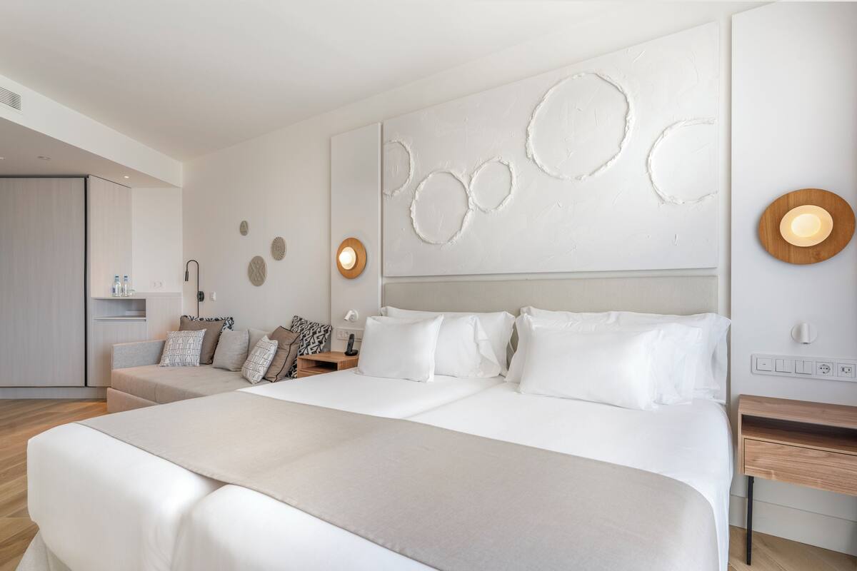 Ein modernes Hotelzimmer mit einem großen Bett, einer Couch, einem Nachttisch und einer Wandleuchte.