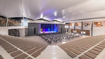 A spacious hall with tiered seating, a stage with colorful lighting, and a modern design with stone accents.