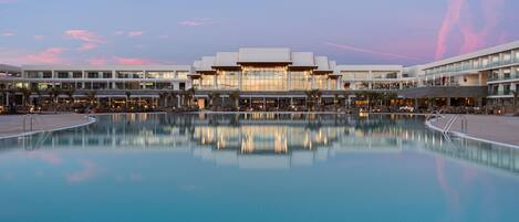 A hotel with a large pool, reflecting the building and sky.
