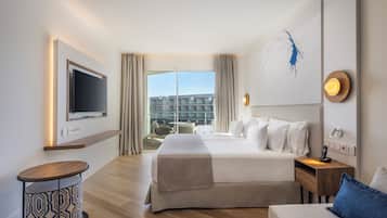 A hotel room with a large bed, a TV mounted on the wall, a bedside table with a lamp, and a view of the city through the window.