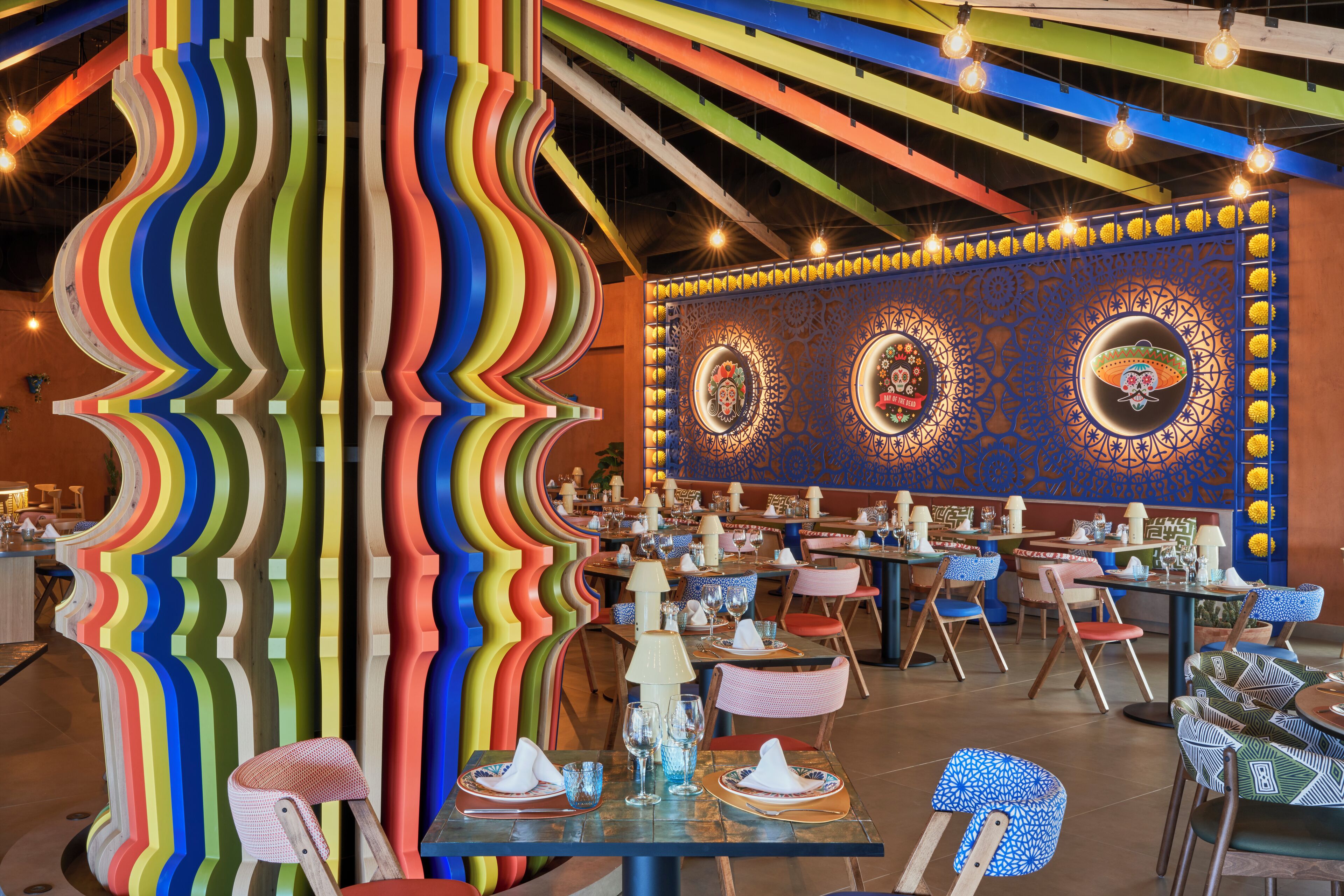 Um restaurante com colunas onduladas coloridas, decoração de parede estampada e mesas preparadas para refeições.