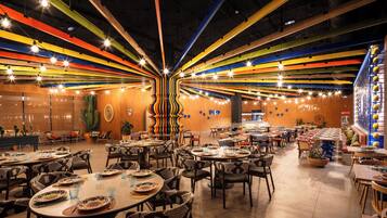 Un restaurante espacioso con varias mesas y sillas, una decoración de cactus y un colorido diseño de techo.
