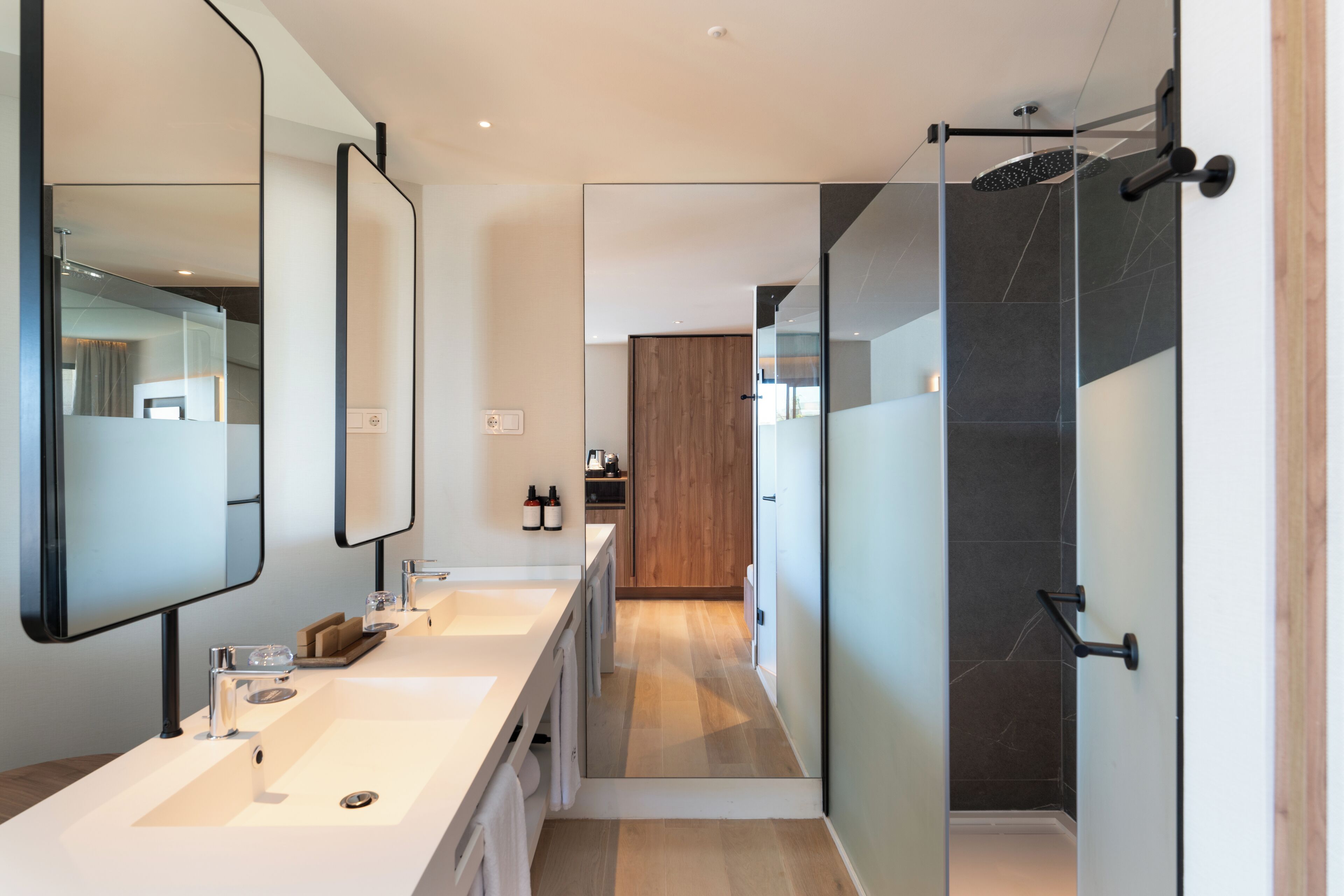 A modern bathroom with a long vanity, a glass shower enclosure, and a wooden cabinet in the background.
