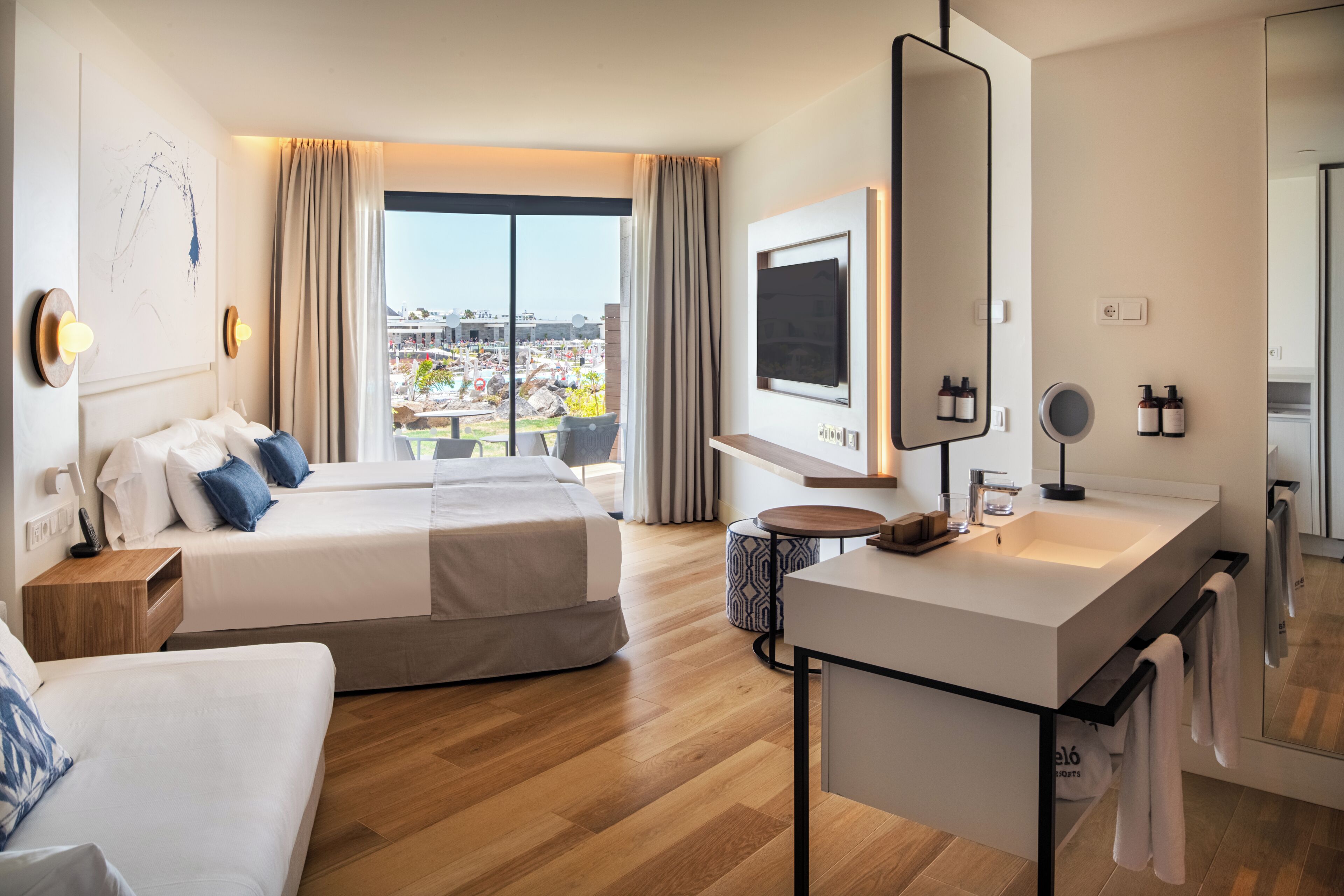 Habitación de hotel con una cama grande, un escritorio, un televisor y un baño con espejo y lavamanos.
