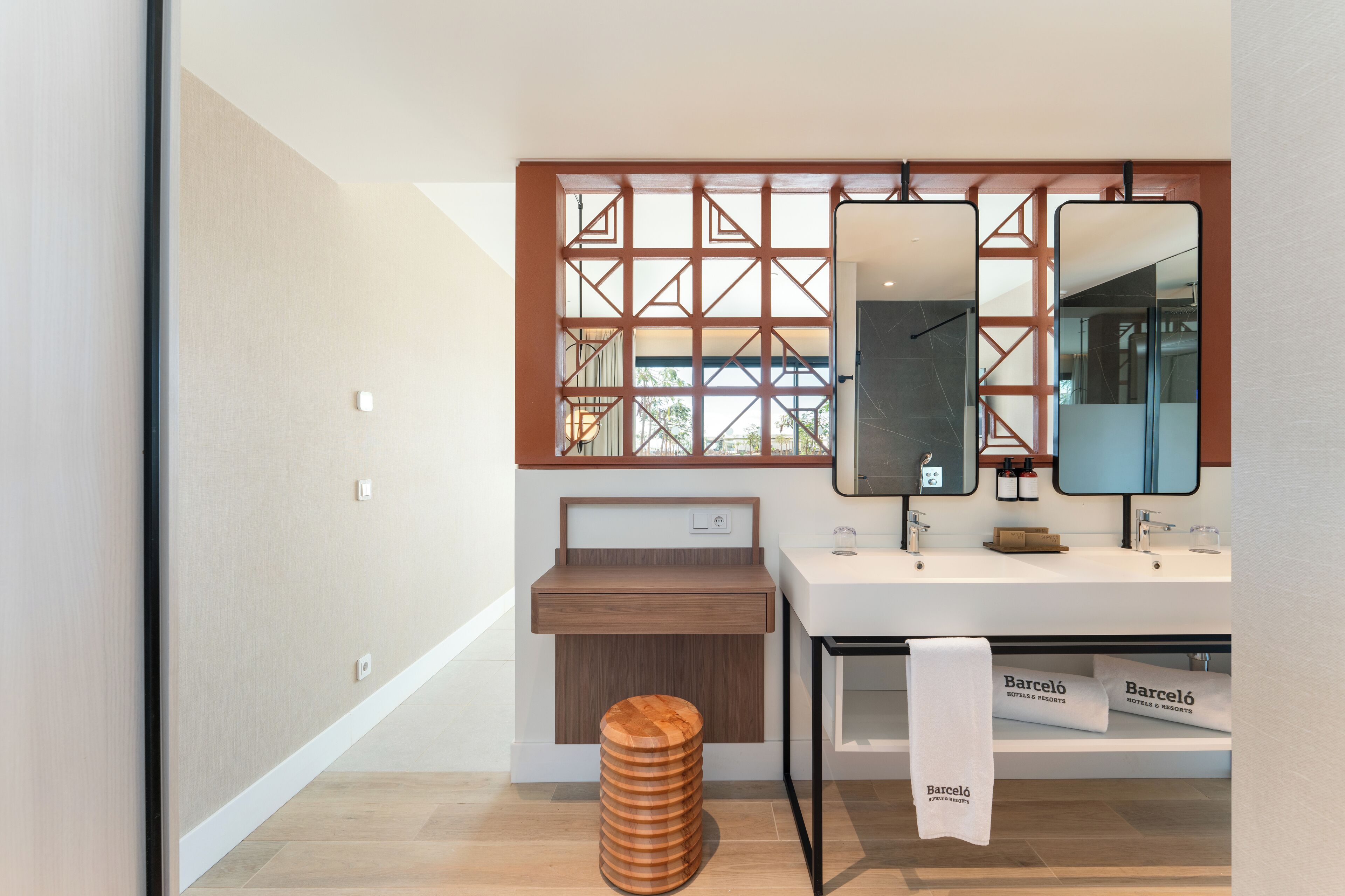 Un baño moderno con un taburete de madera, un espejo grande y una ventana con diseño geométrico.