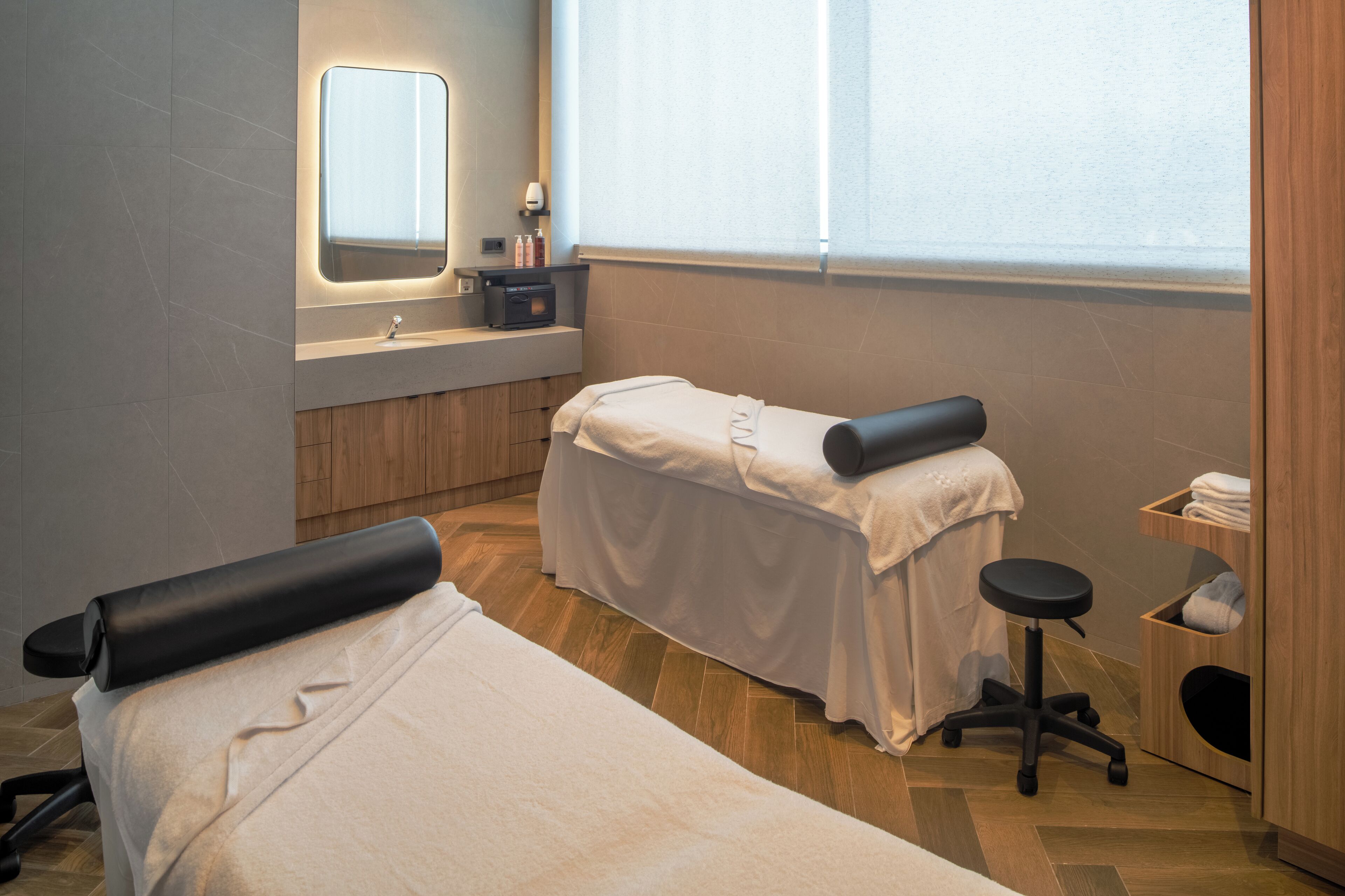 A clean, modern spa room with a massage table, a small sink, and a mirror.
