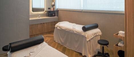 A clean, modern spa room with a massage table, a small sink, and a mirror.