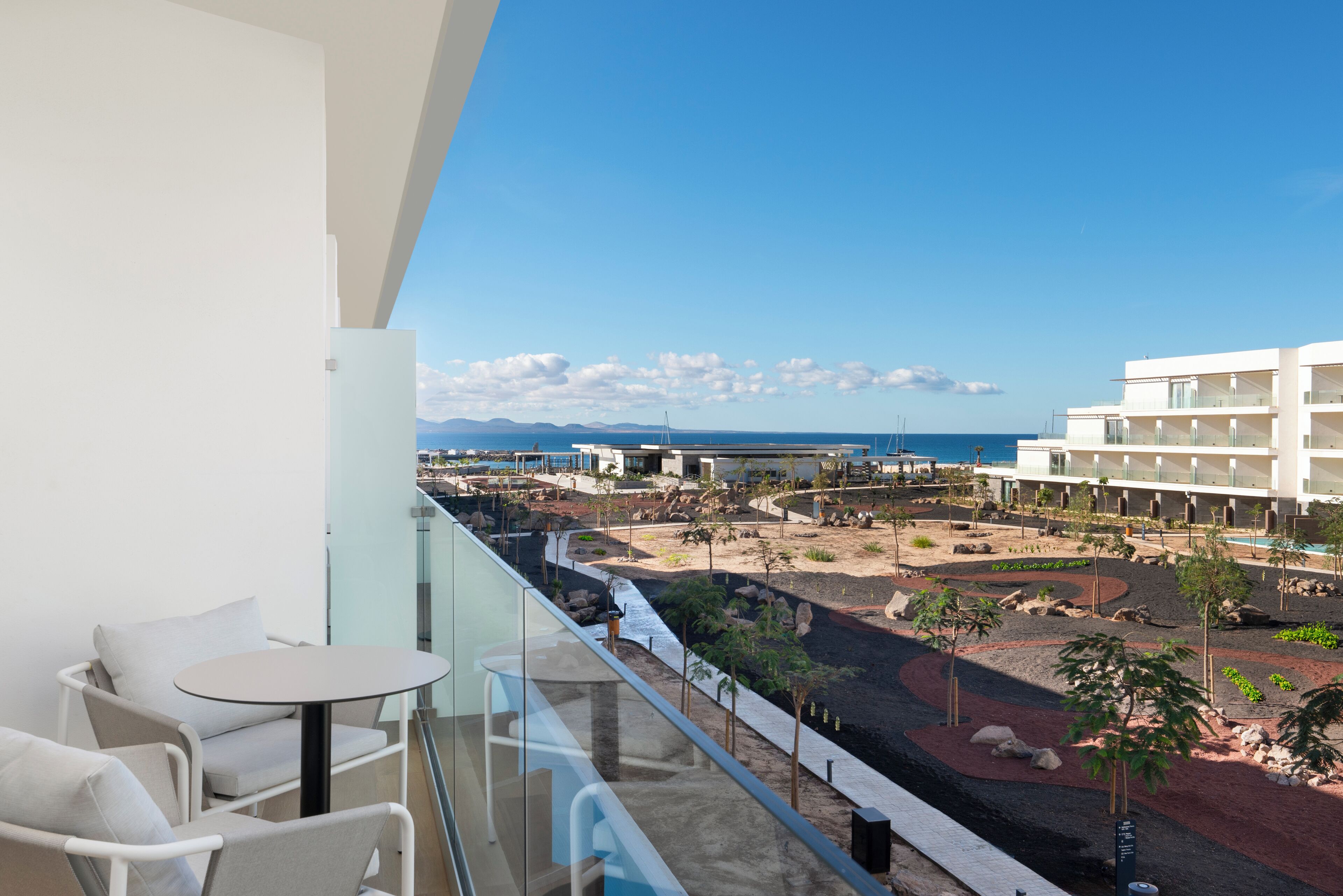 A balcony with a view of a landscaped area, a pool, and a building in the background.